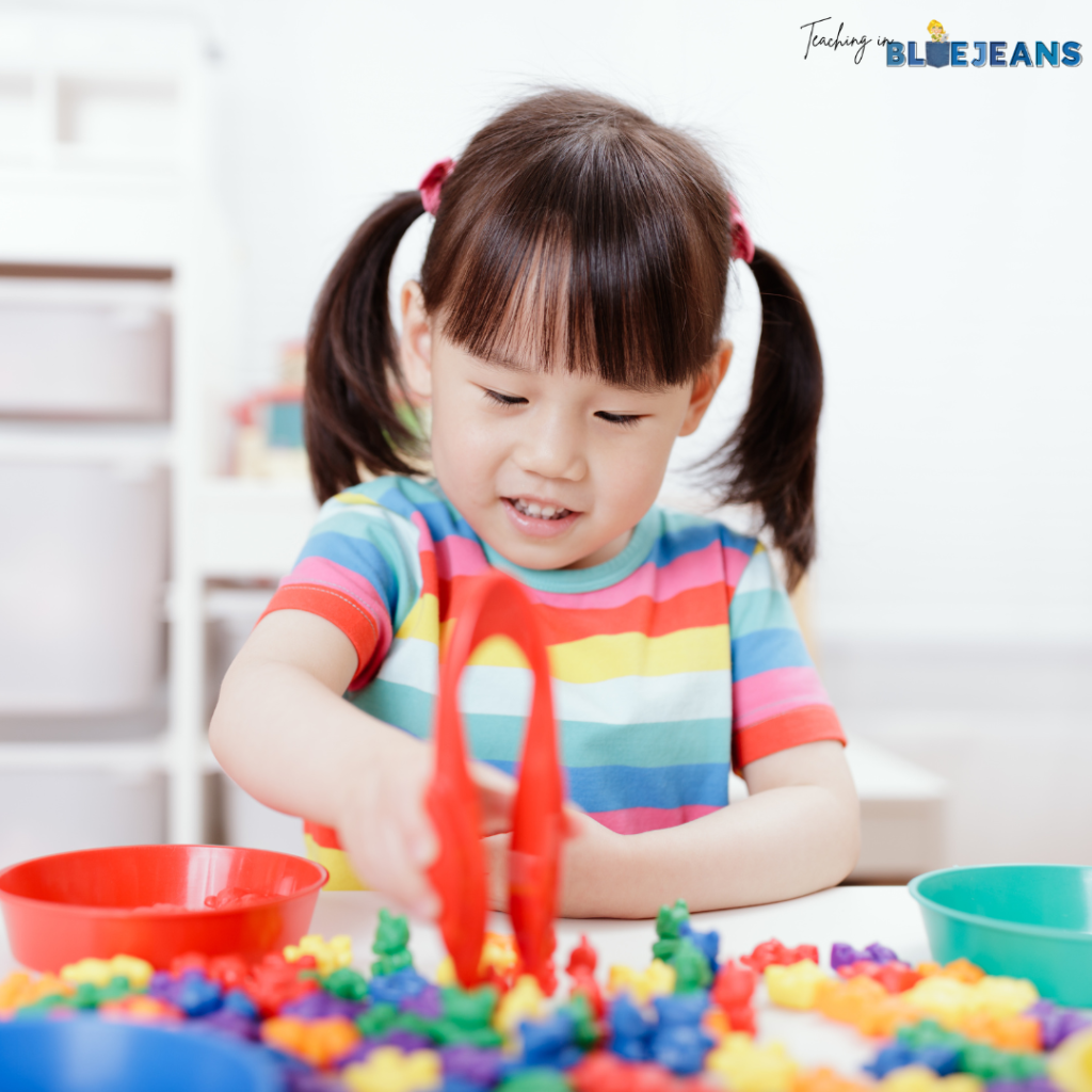 In this image, a child is using tongs to sort bear shaped manipulatives into bowls.